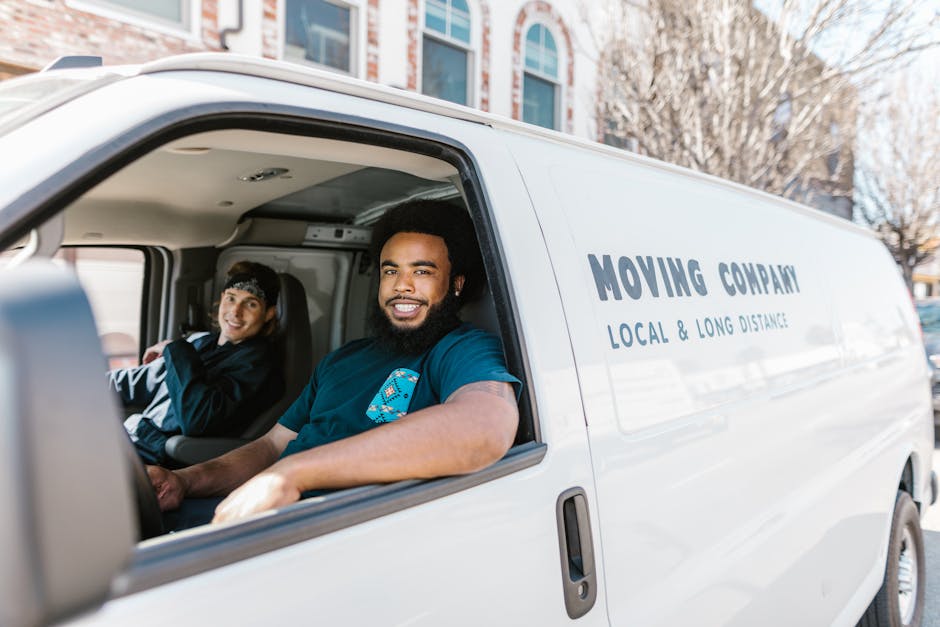 The image shows a man with glasses and a beard wearing a white polo shirt, standing outside a moving van during a home relocation, with the van's open rear door revealing the interior filled with pack
